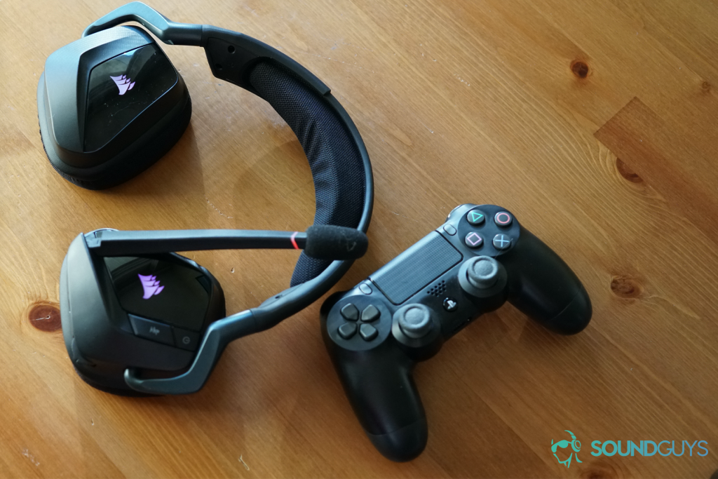 The Corsair Void RGB Elite Wireless gaming headset sits on a wooden table next to a Dualshock controller for the Sony Playstation 4