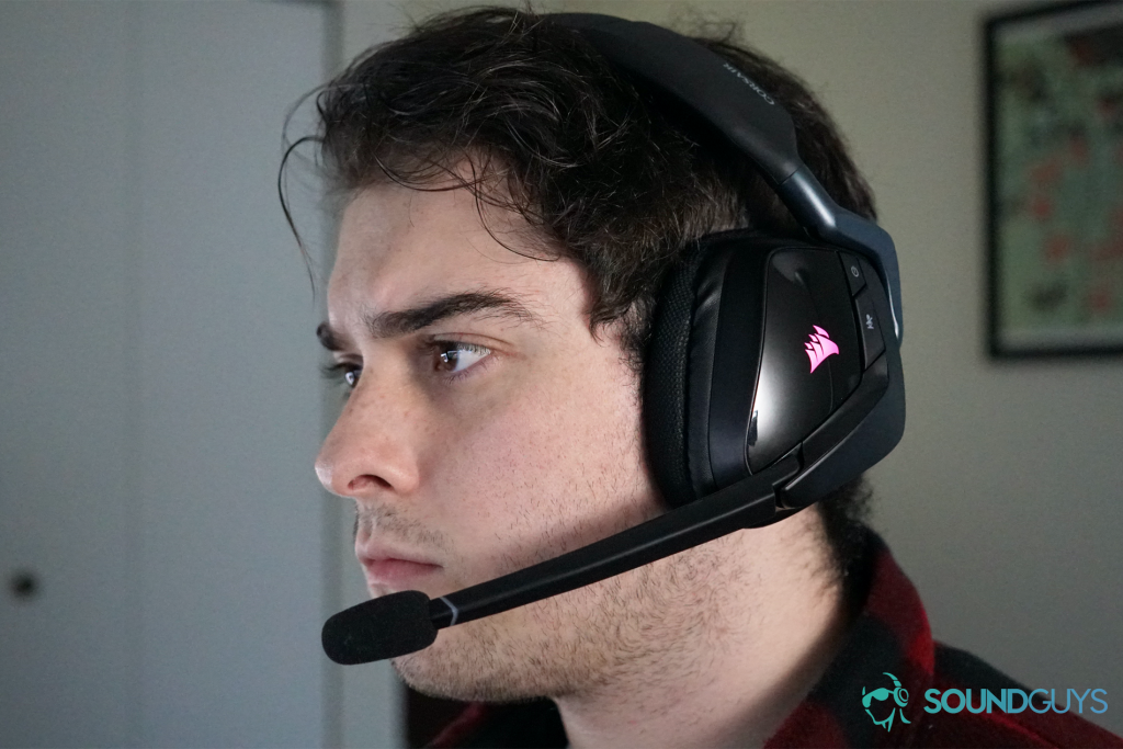 A man wearing the Corsair Void RGB Elite Wireless gaming headset with posters in the background.