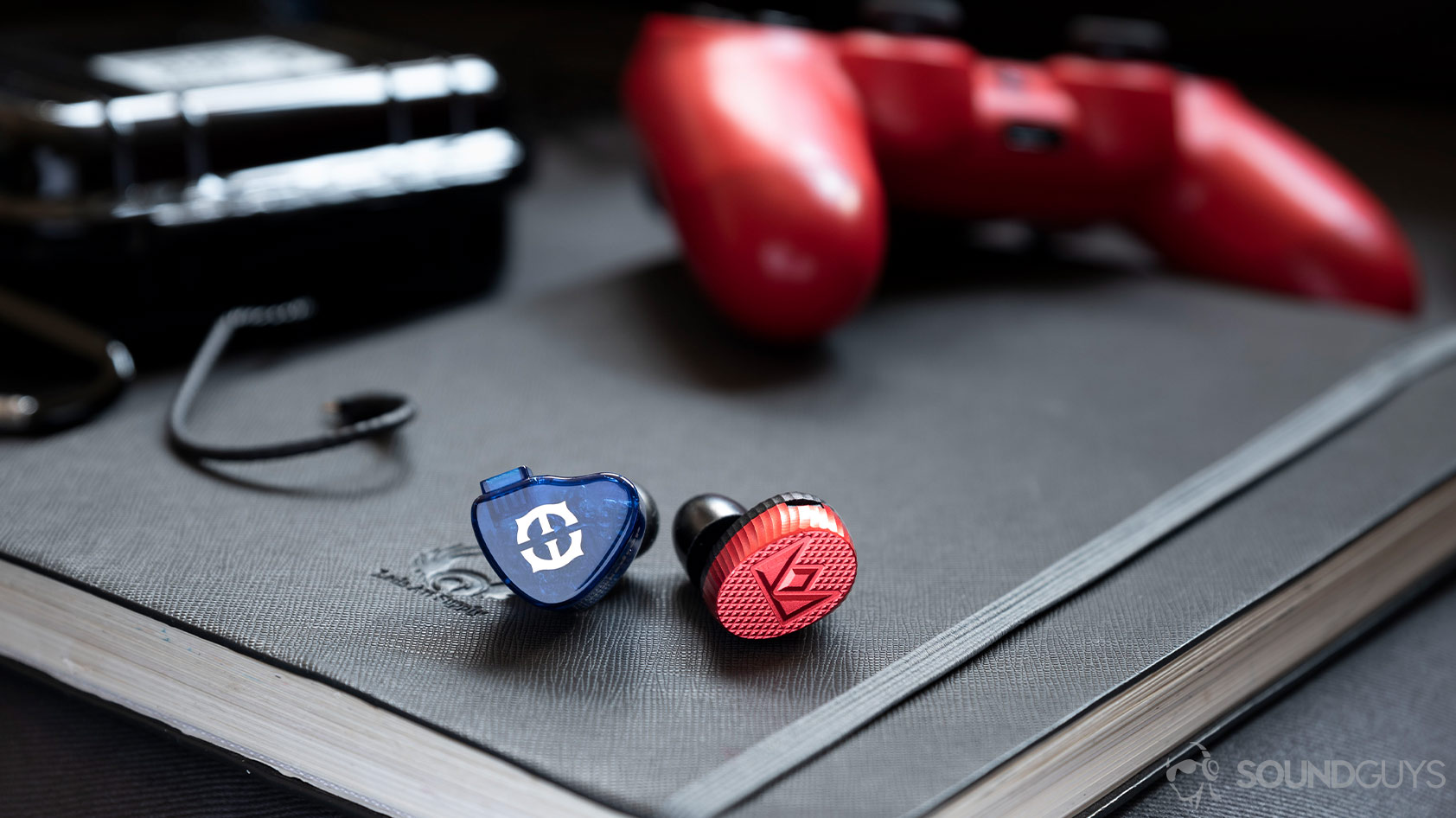 A photo of the Massdrop x Empire Ears Zeus and Massdrop x Noble Audio Kaiser 10 in-ear monitors next to each other with a PS4 controller in the background.