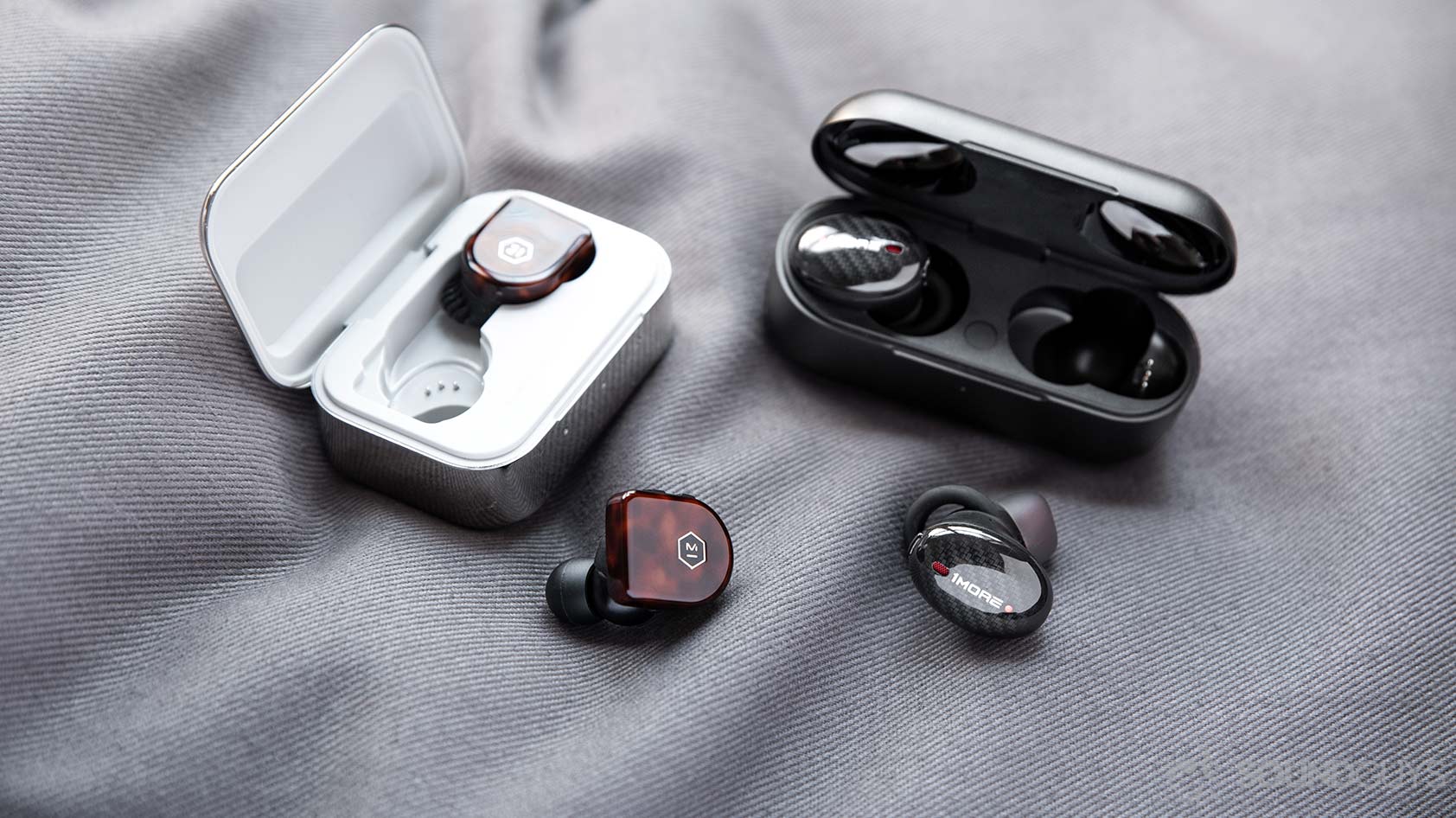 A picture of the 1More True Wireless ANC and Master &amp; Dynamic MW07 noise canceling true wireless earphones and their respective charging cases; both headsets are pricier than the 1More Stylish True Wireless.