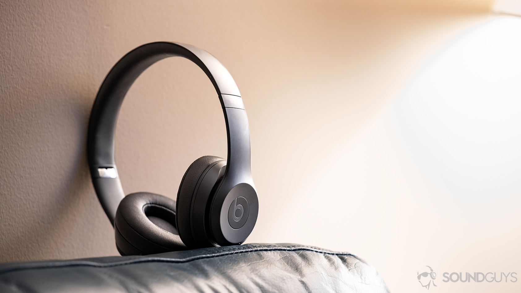 The Beats Solo3 Wireless headphones standing on a couch against a warm-tinted wall.