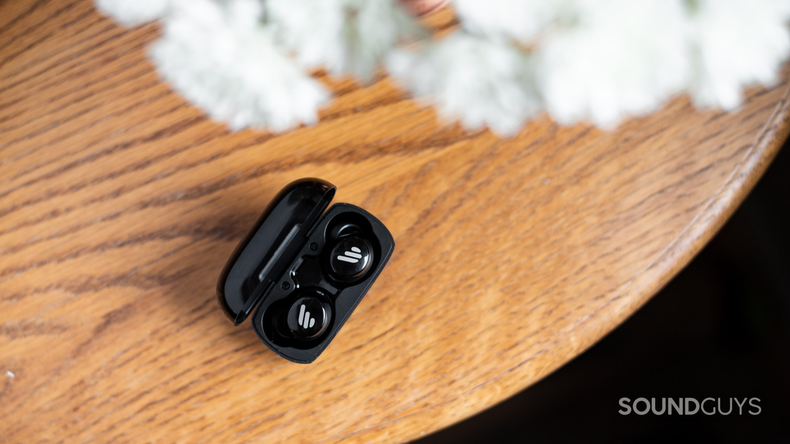 An aerial picture of the Edifier TWS1 true wireless earbuds in the charging case on a wood surface.
