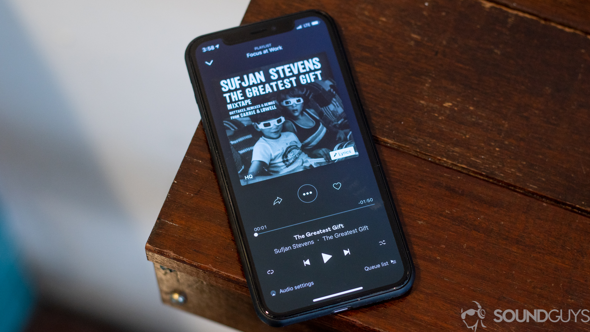 Pictured is the main playing now section of the Deezer app on an iPhone 11 Pro on wood table.