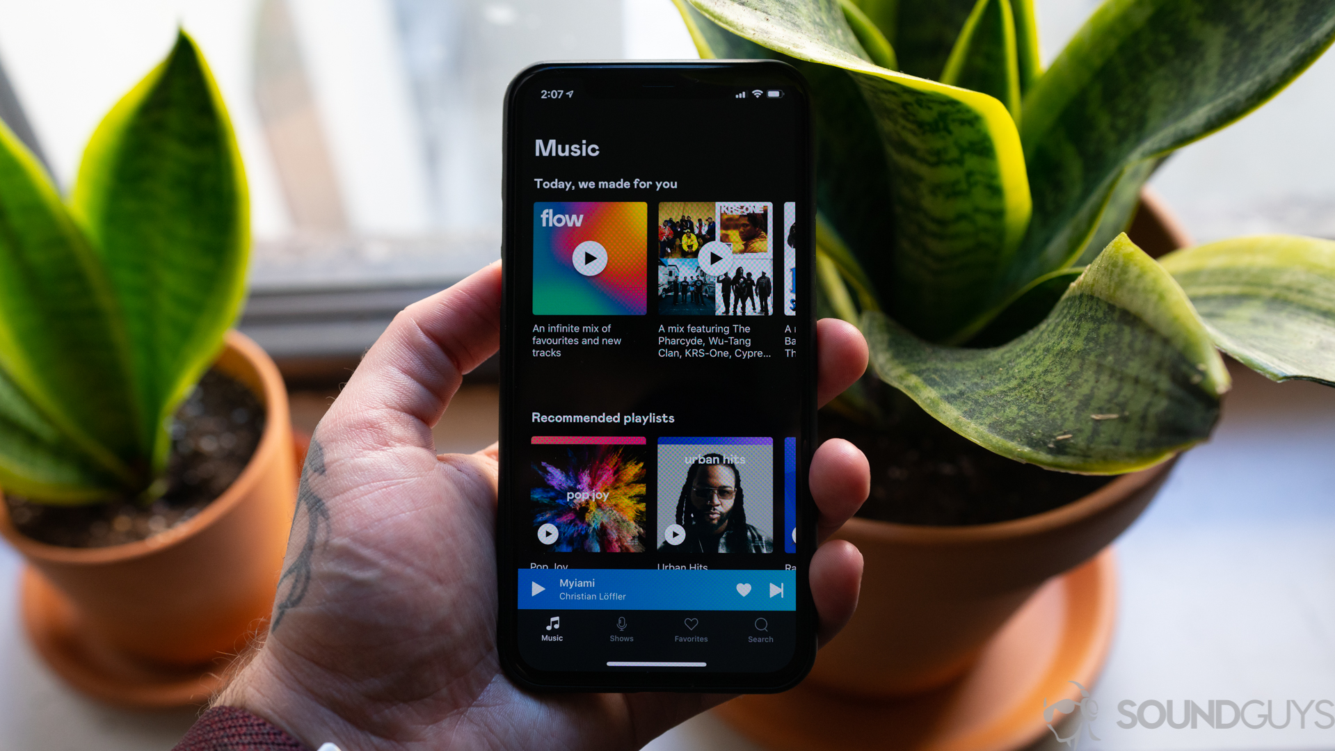 An iPhone 11 Pro in hand in front of plants showing off the main music page of the Deezer app