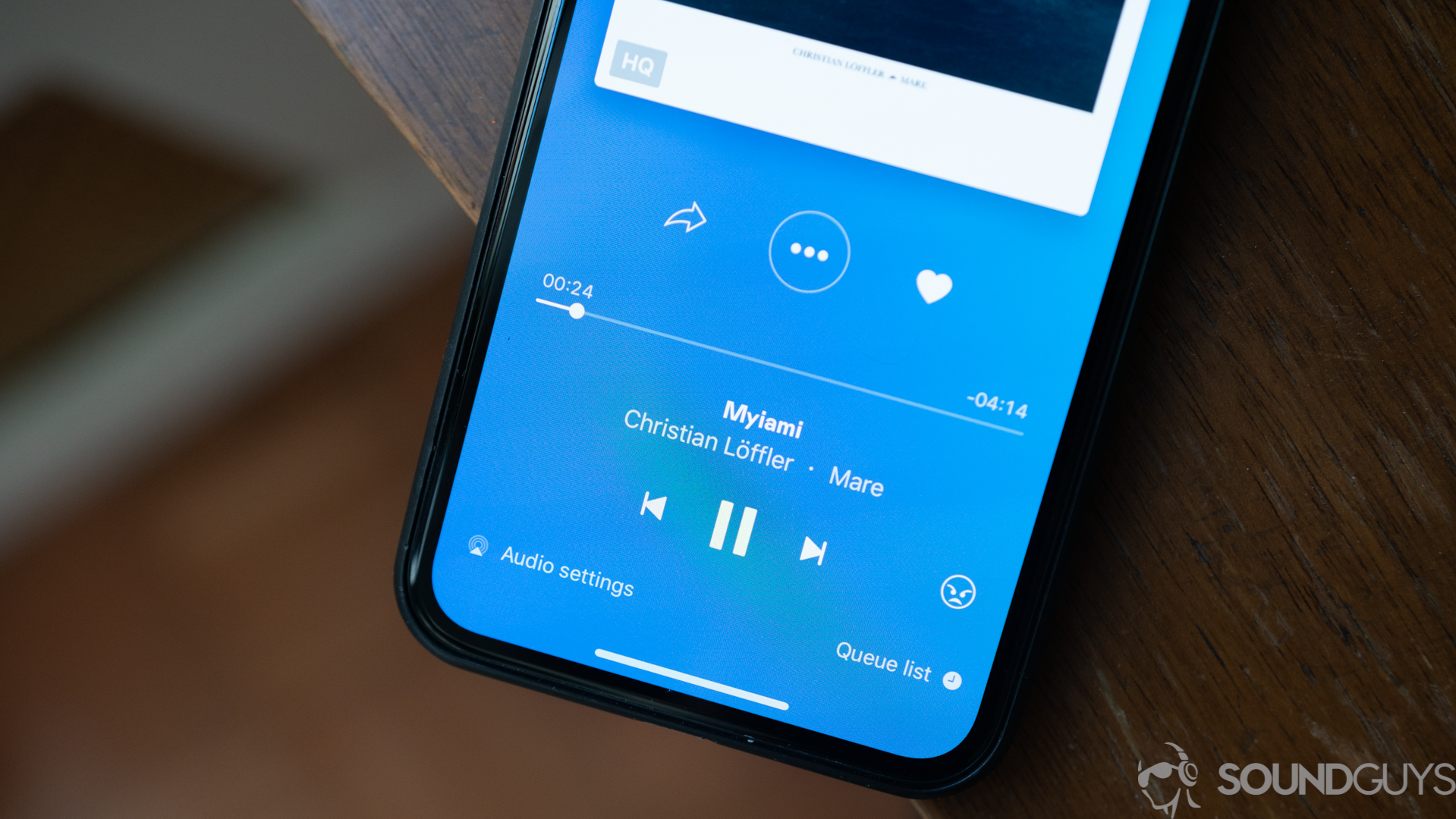 Shot of playback controls and UI of Deezer app on an iPhone on wood table.