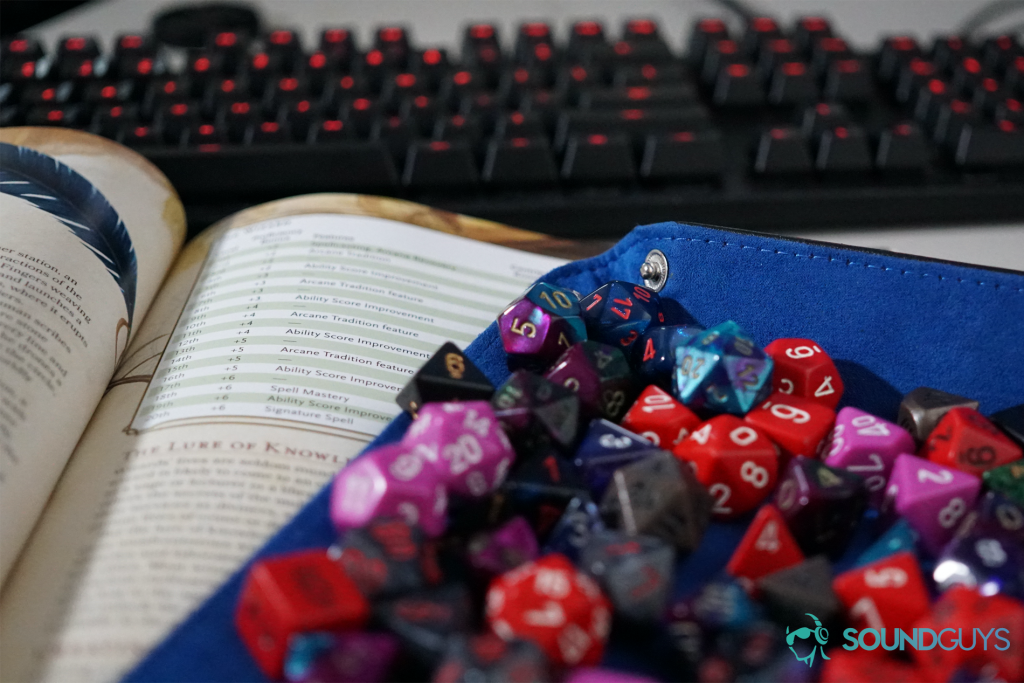 polyhedral dice sit on top of an open Dungeons and Dragons Players Handbook in front of a Logitech keyboard on a table.