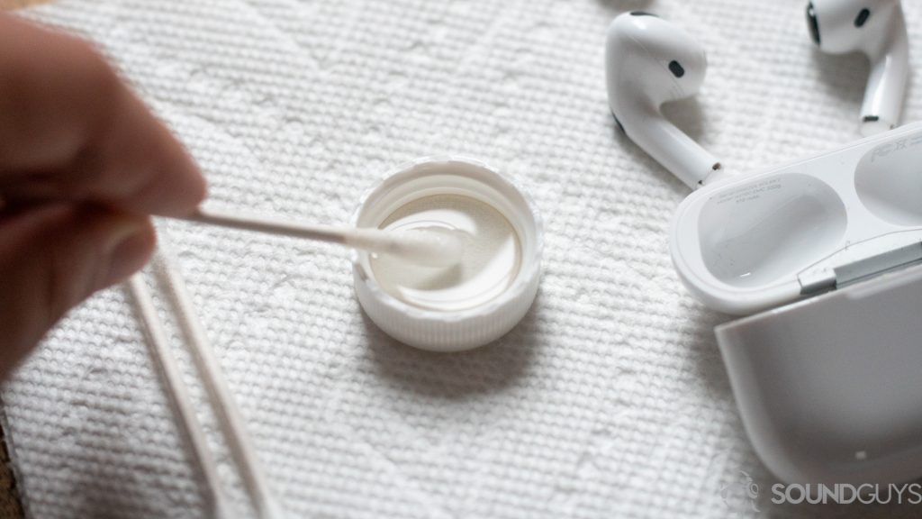 A photo of the AirPods Pro, about to be cleaned with a Q-tip (foreground) and alcohol.