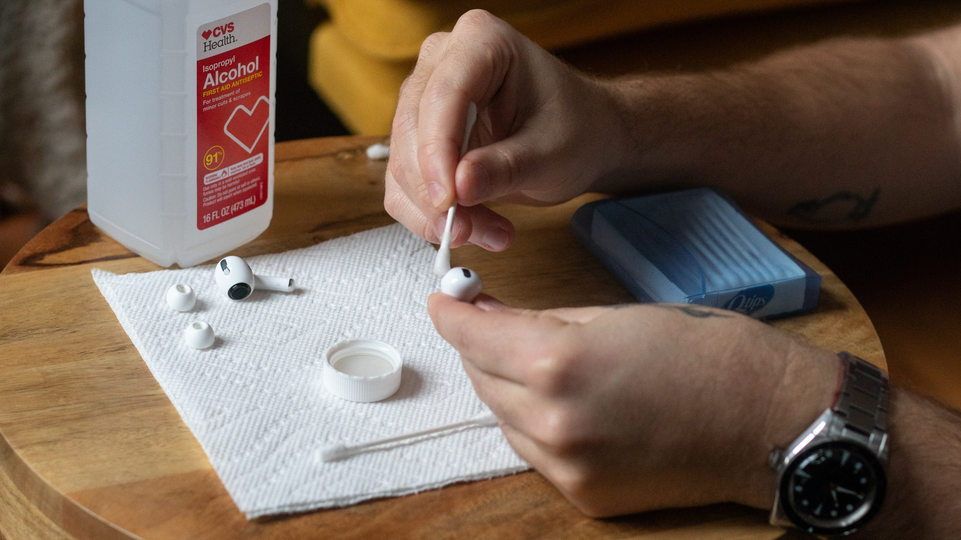 A man holds a Q-tip to a pair of AirPods Pro earbuds as he cleans them with isopropyl alcohol.