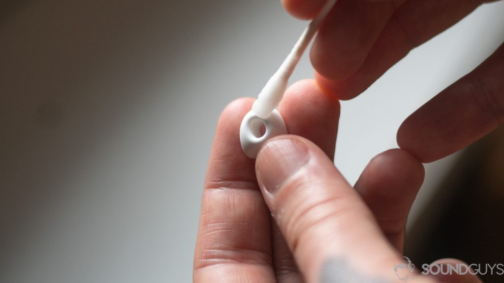 Man holding Q-tip to white ear tip, illustrating how to clean headphones.