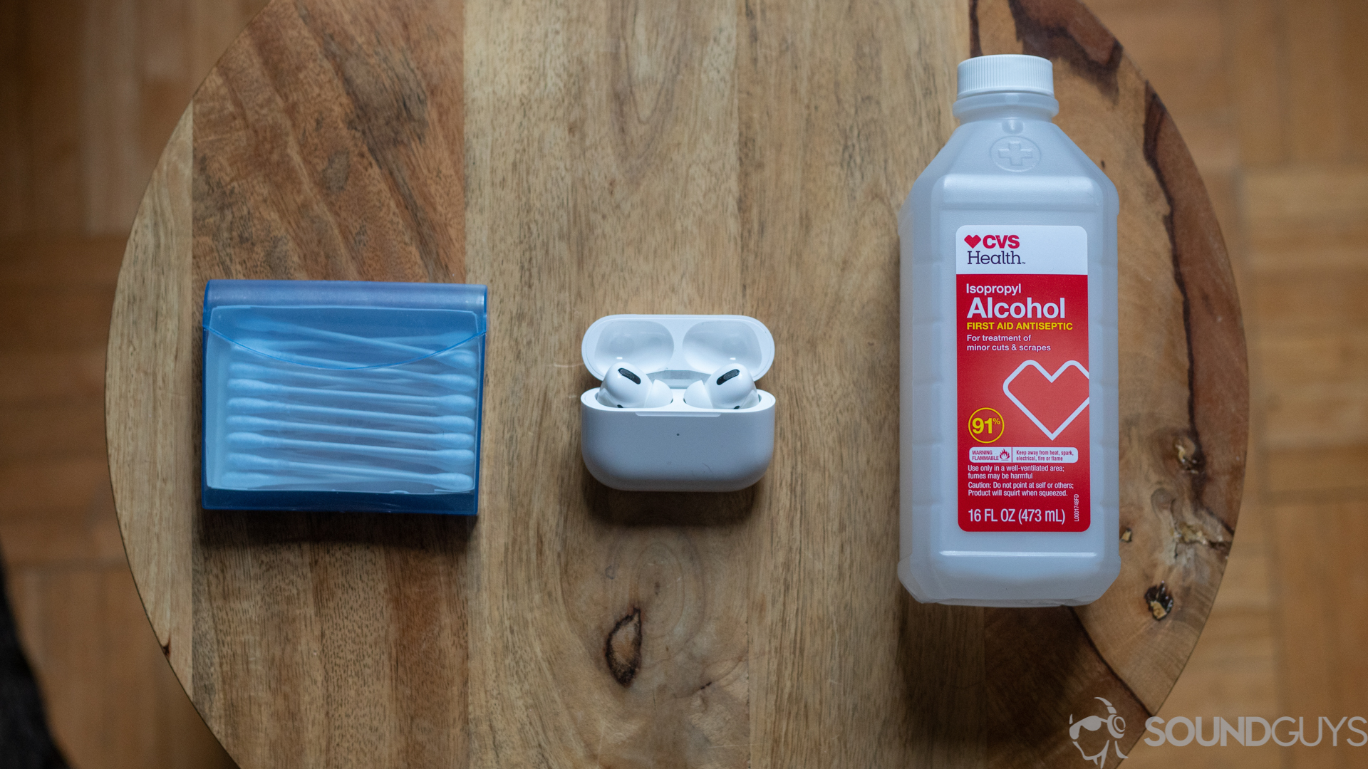 A photo of AirPods Pro, alcohol, and q-tips on a wooden desk.