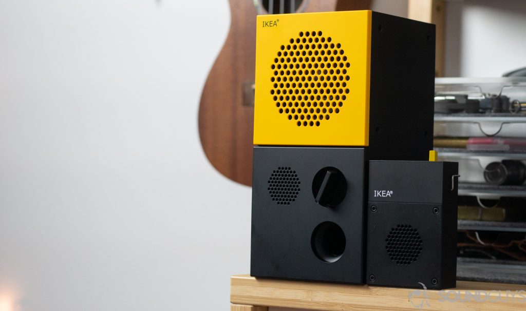 Yellow and black IKEA x Teenage Engineering speakers next to each other on a desk with ukulele in the background.