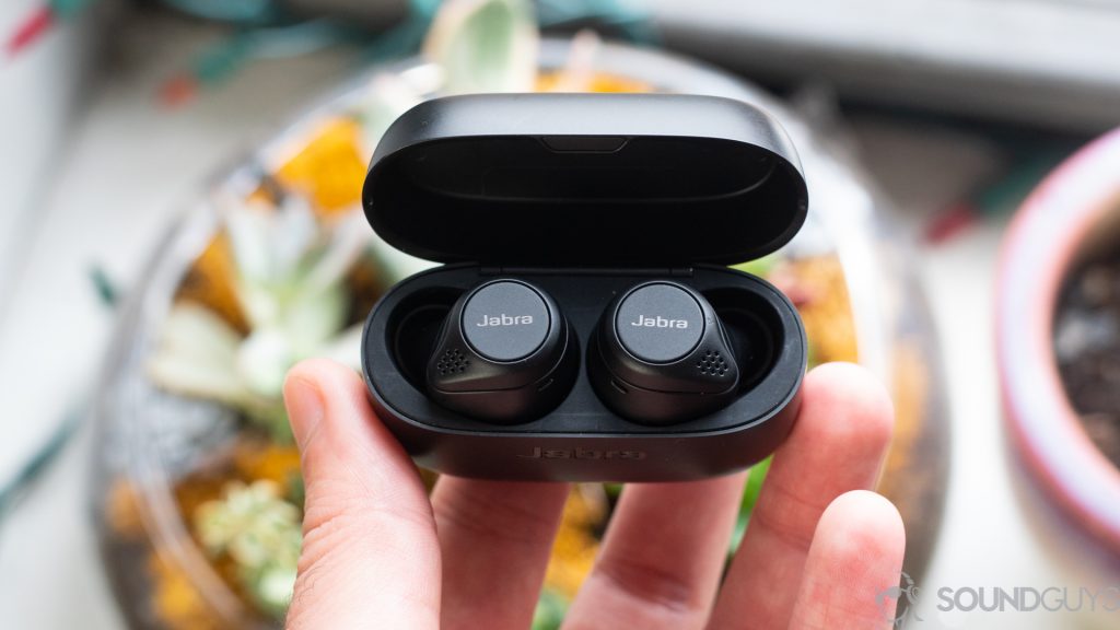 Man holding Jabra Elite 75t earbuds with case open over plants