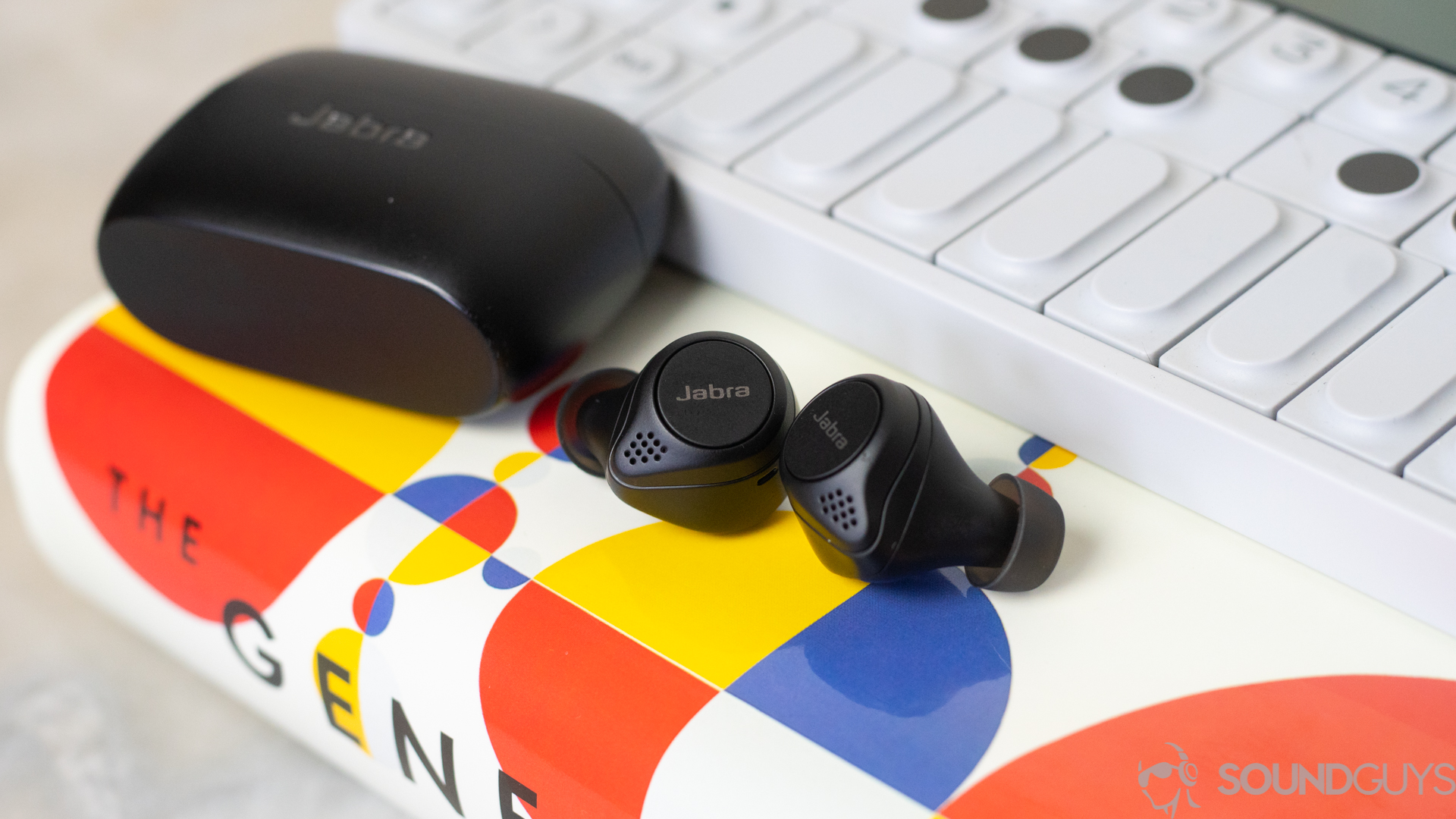 The Jabra Elite 75 earbuds on top of a book and next to synthesizer