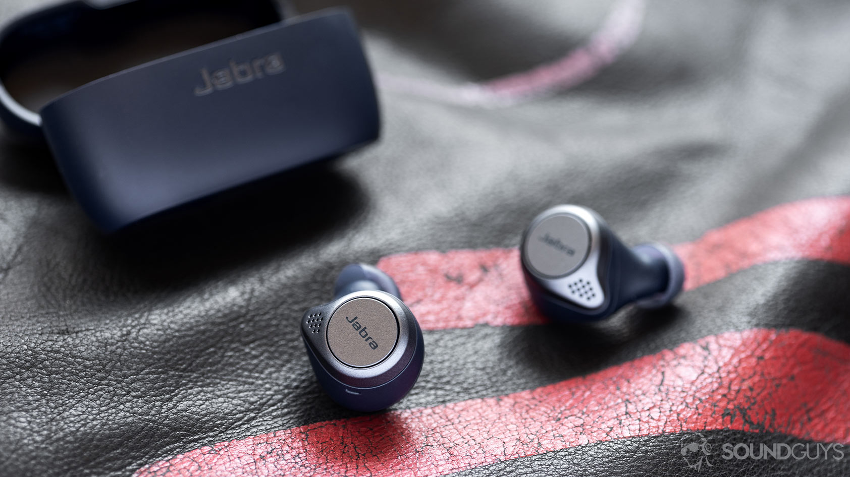 Jabra Elite Active 75t-true wireless workout earbuds case A picture of the Jabra Elite Active 75t true wireless workout earbuds (navy) on a leather surface with the charging case open in the background.
