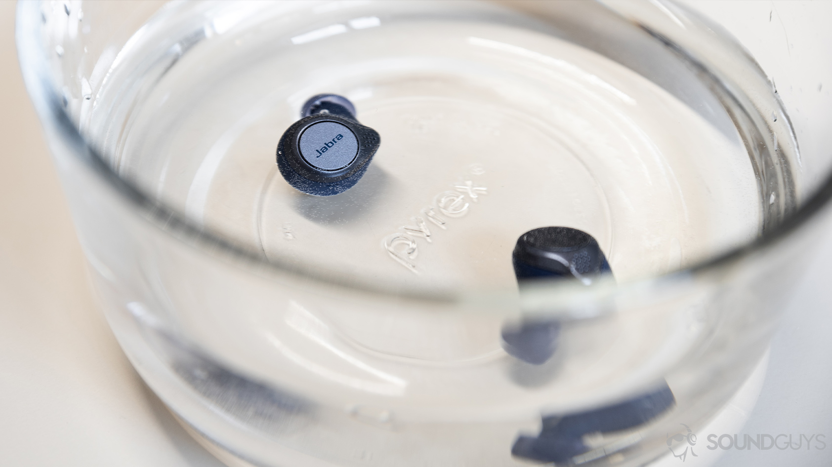 A picture of the Jabra Elite Active 75t true wireless workout earbuds (navy) submerged in a Pyrex bowl of water.