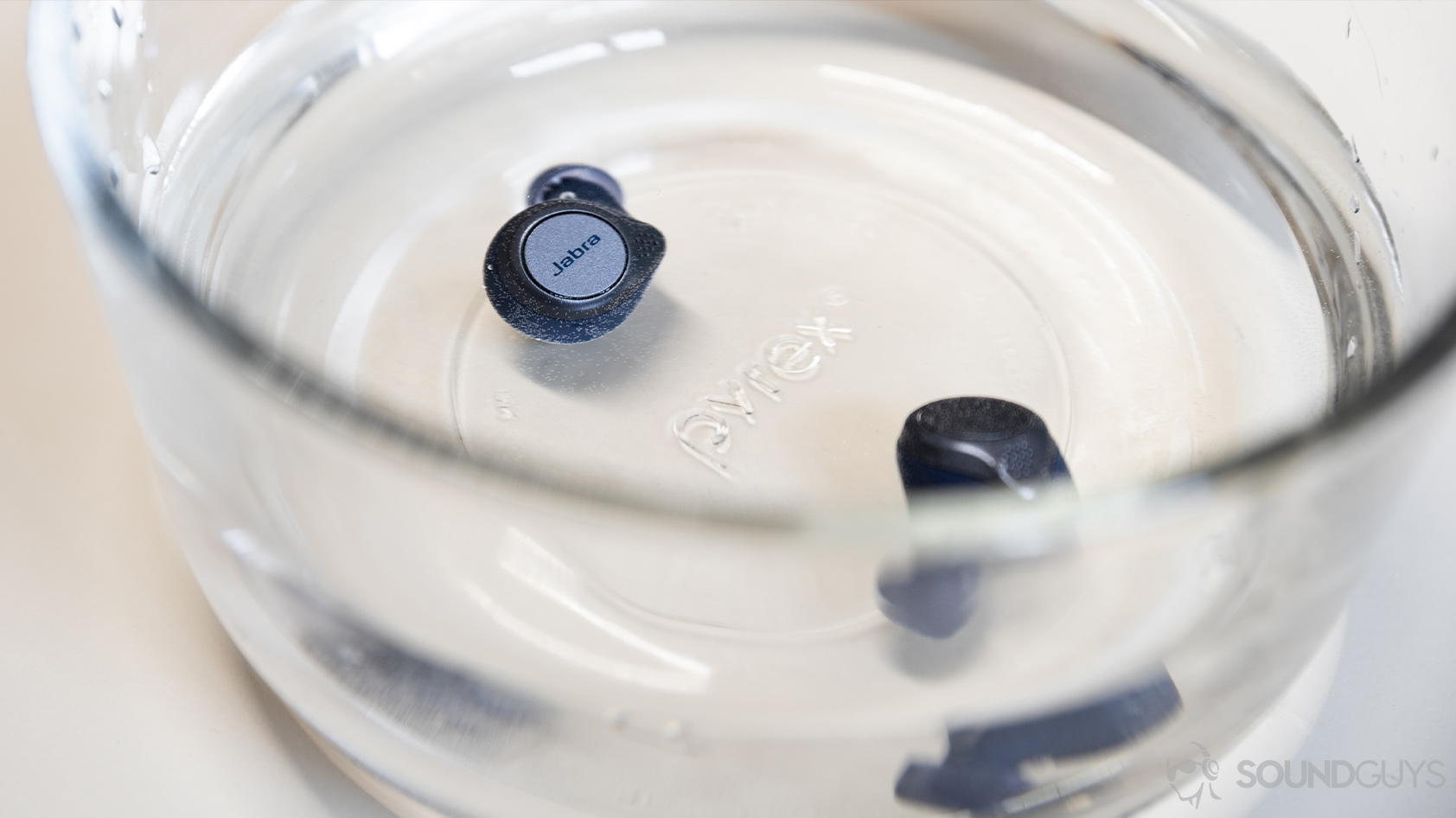 The Jabra Elite Active 75t true wireless workout earbuds (navy) submerged in a Pyrex bowl of water.