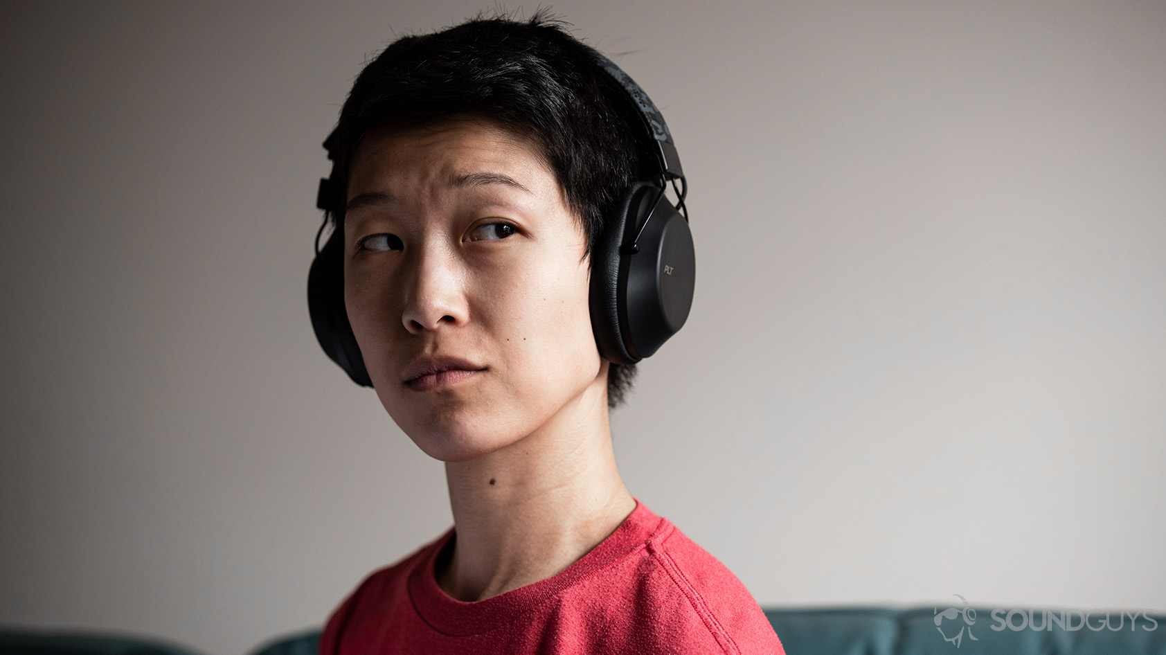 A woman wears the Plantronics BackBeat Fit 6100 workout headphones against an off-white wall.