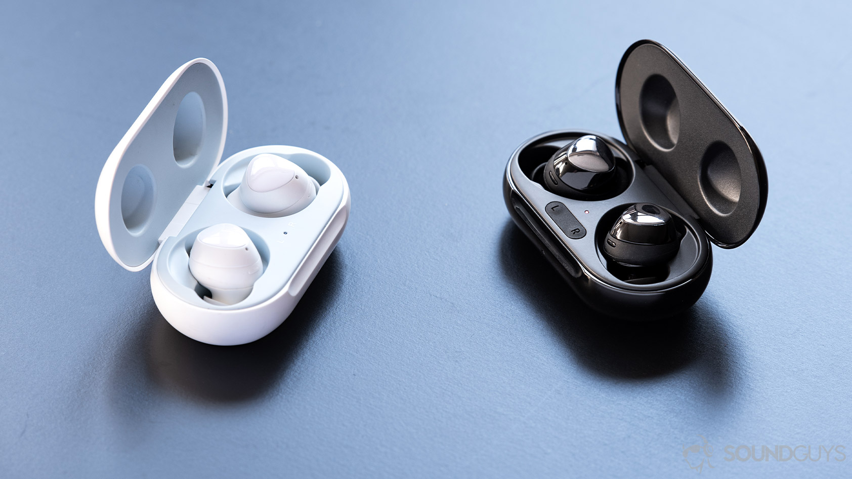 A comparison/versus picture of the Samsung Galaxy Buds Plus and Galaxy Buds in their respective cases, angled toward each other.