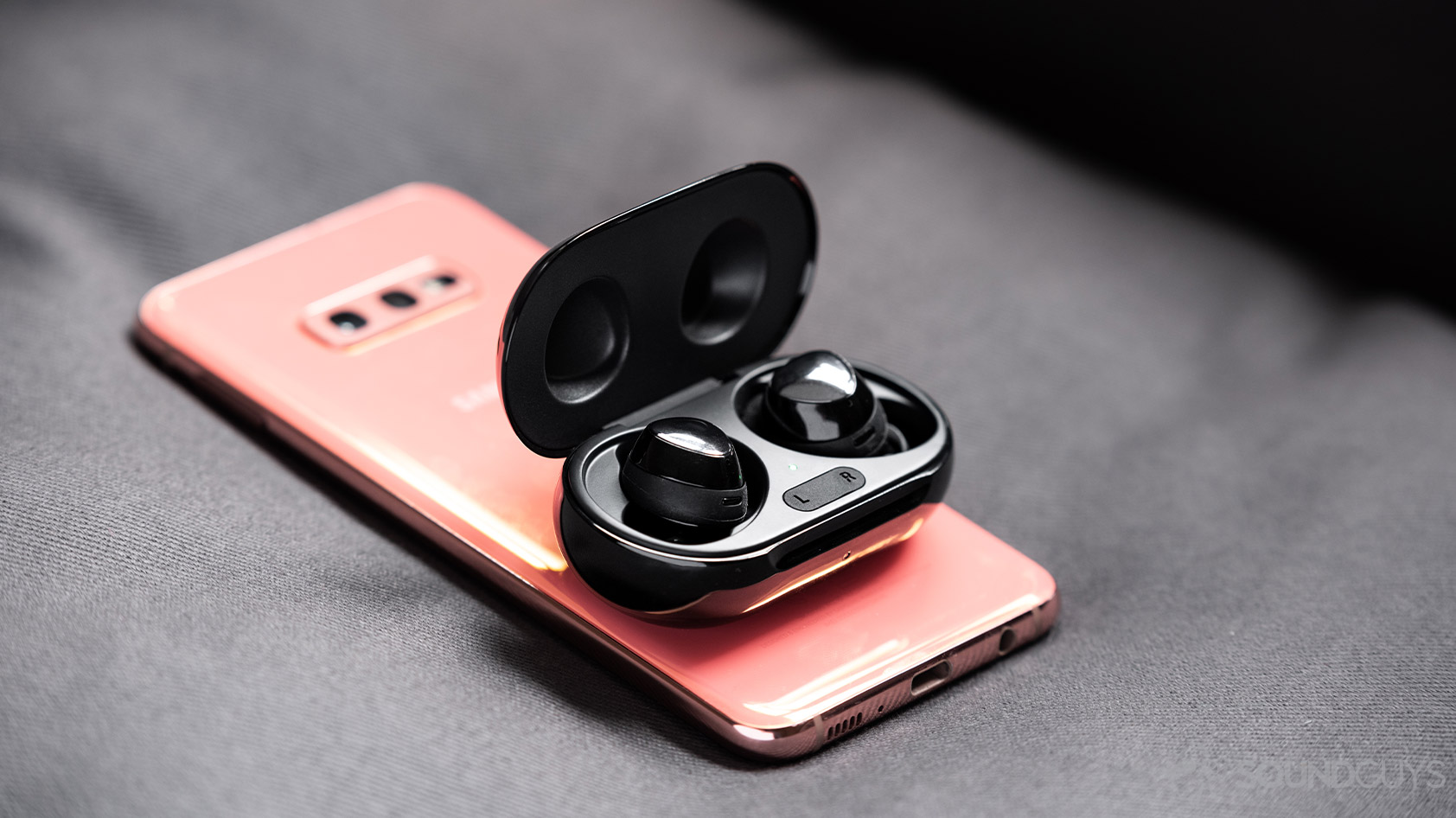 The Samsung Galaxy Buds Plus true wireless earbuds on top of a Samsung Galaxy S10e smartphone in flamingo pink.