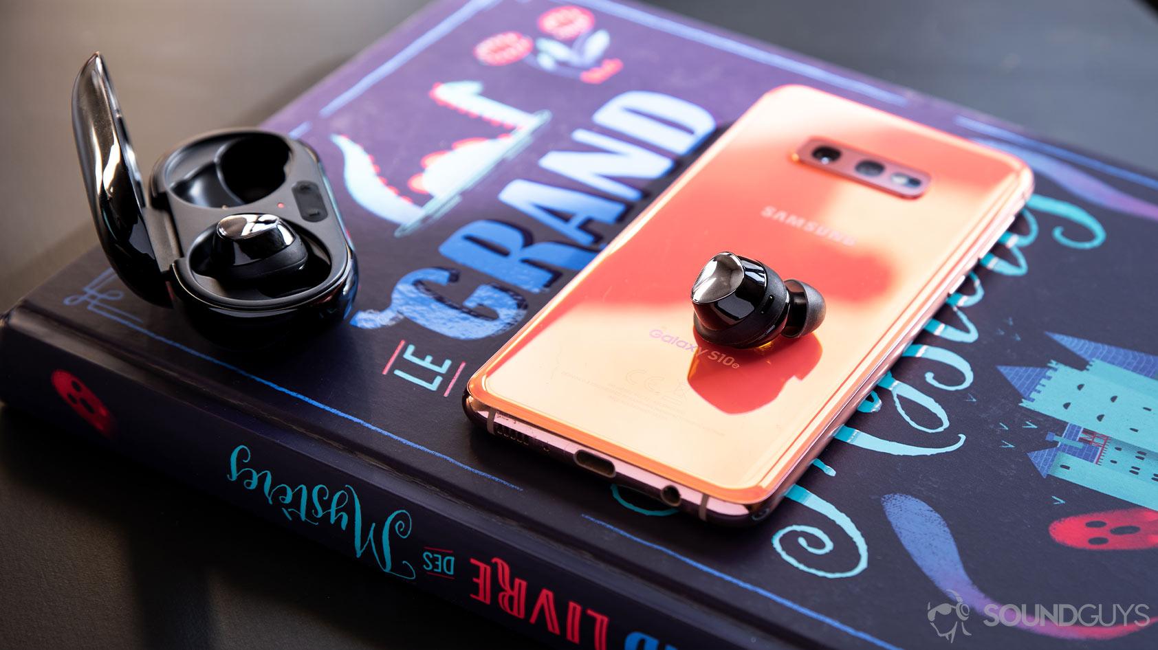 A picture of the Samsung Galaxy Buds Plus earbud atop a Galaxy S10e smartphone with the charging case open and off to the left-side of the frame.