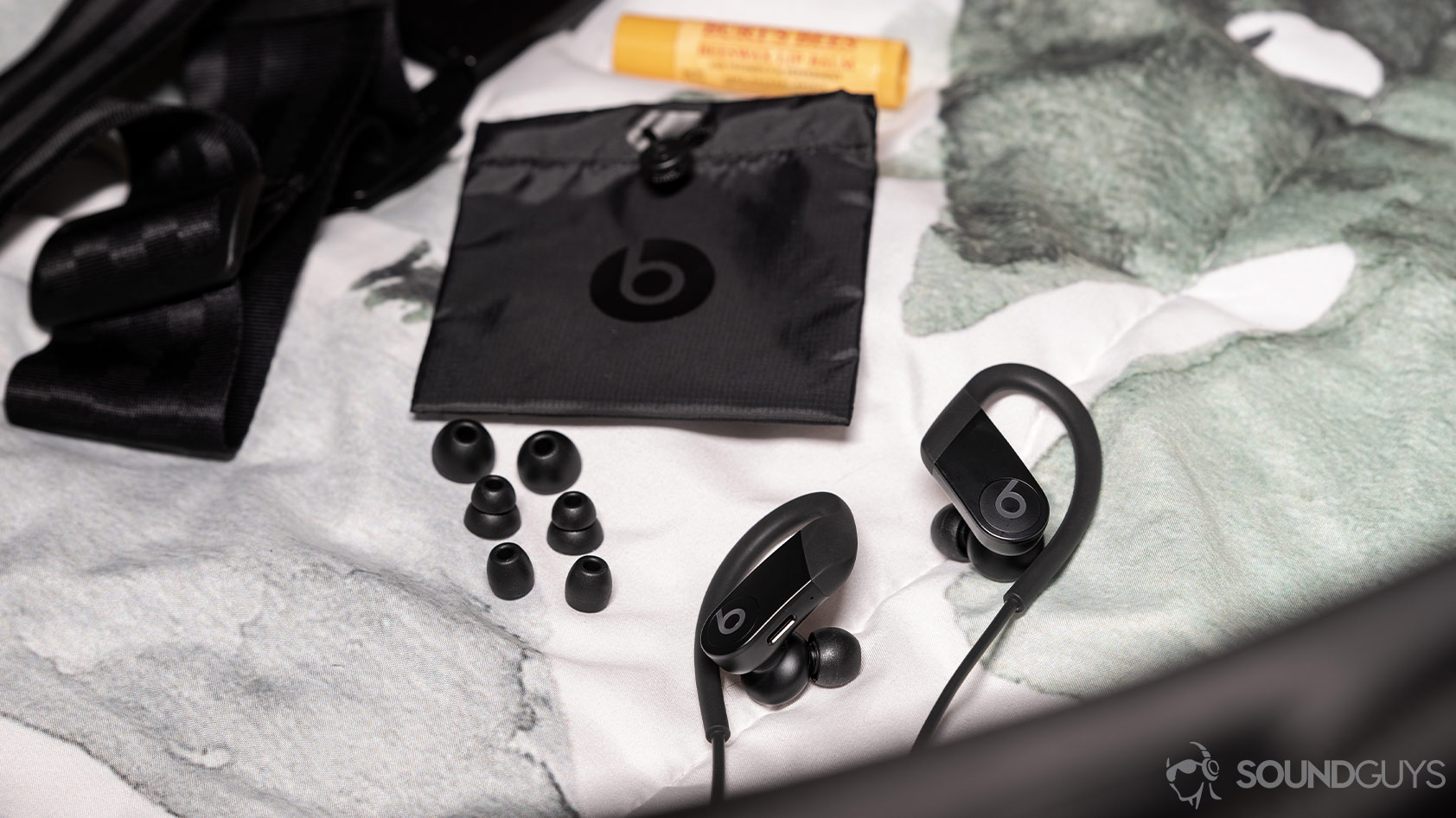 A picture of the Apple Beats Powerbeats workout earbuds, spare ear tips, and carrying pouch on a white and green comforter.