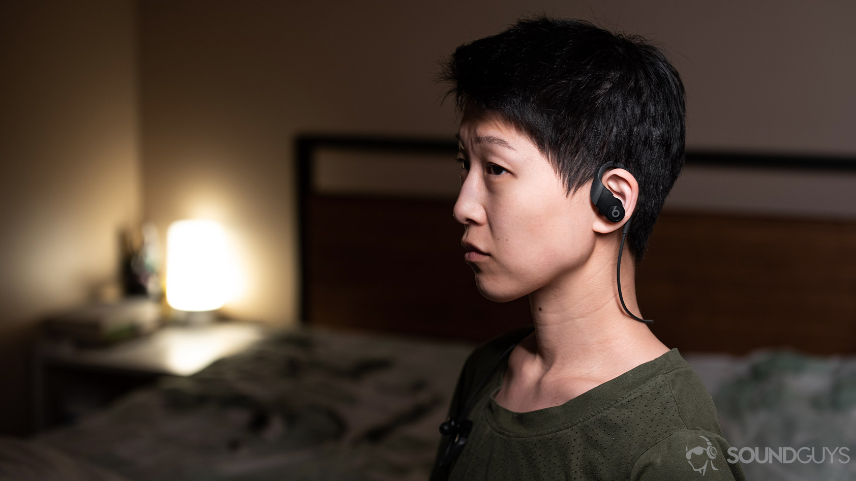 A picture of a woman wearing the Apple Beats Powerbeats workout earbuds in a bedroom.