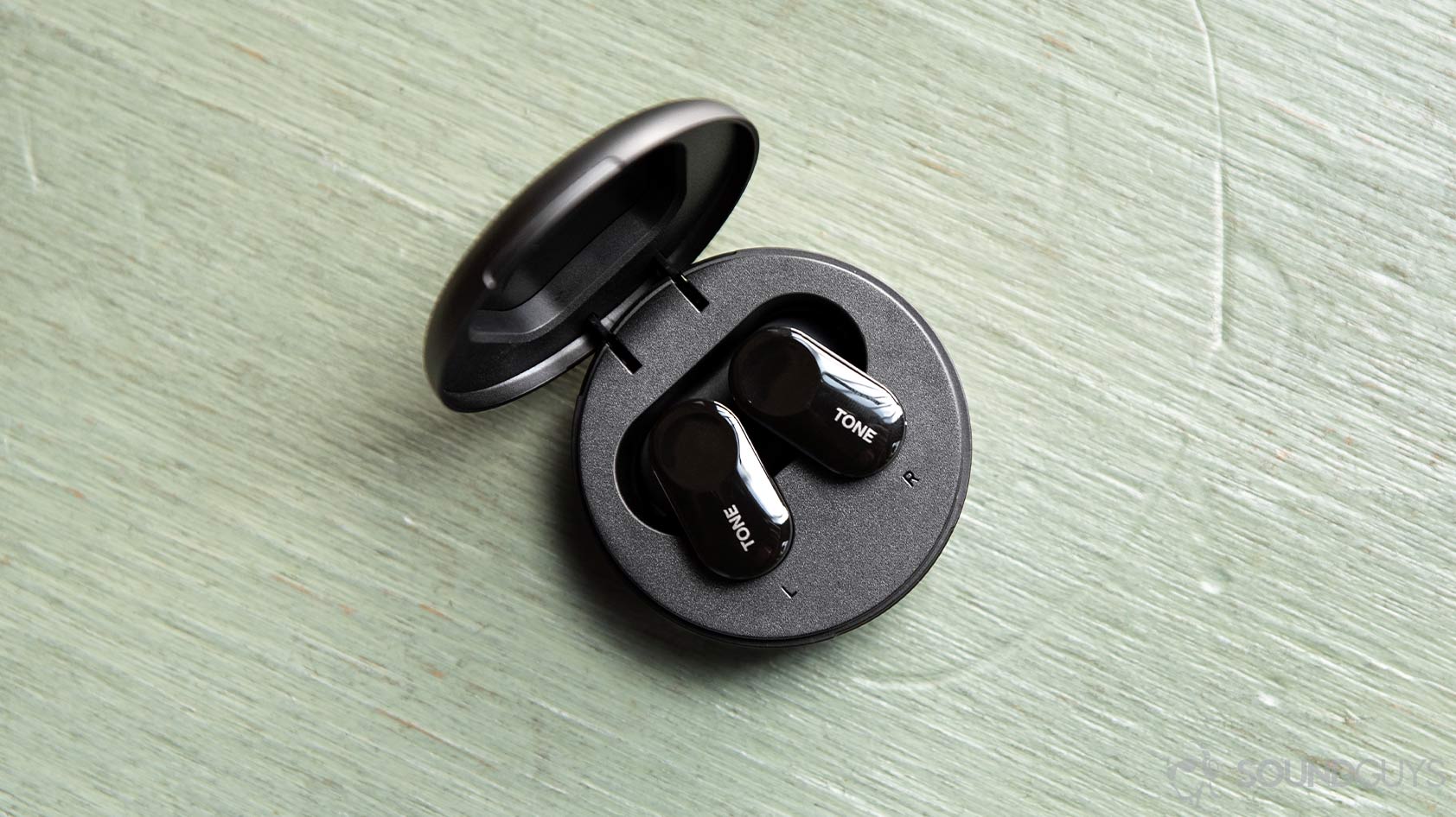 An aerial photo of the LG Tone Free HBS FL7 true wireless earbuds in the circular charging case on a green wood surface.