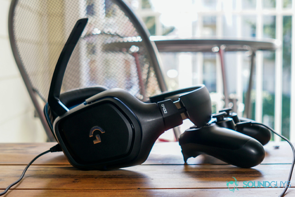 The Logitech G432 leans on a Playstation 4 controller on a wooden table in front of some metal folding chairs.