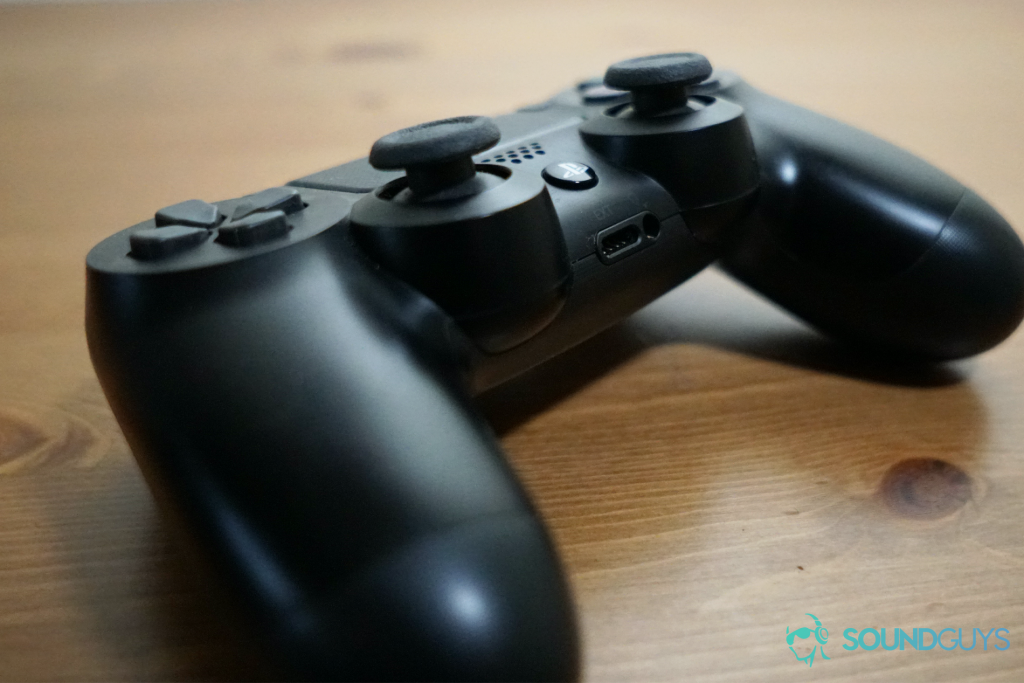 A photo of a Sony PlayStation 4 dual-shock controller sitting on a wooden desk, showing the 3.5mm analog TRRS port on the front.