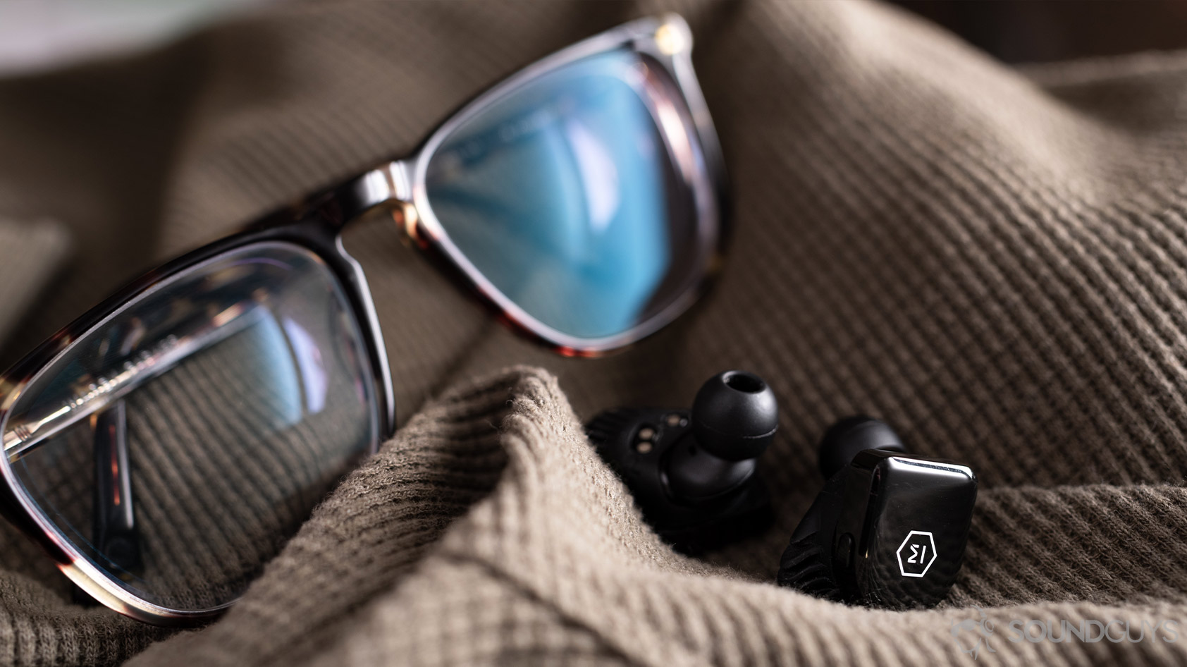 A picture the Master &amp; Dynamic MW07 Go true wireless earbuds in front of Warby Parker tortoise shell glasses.