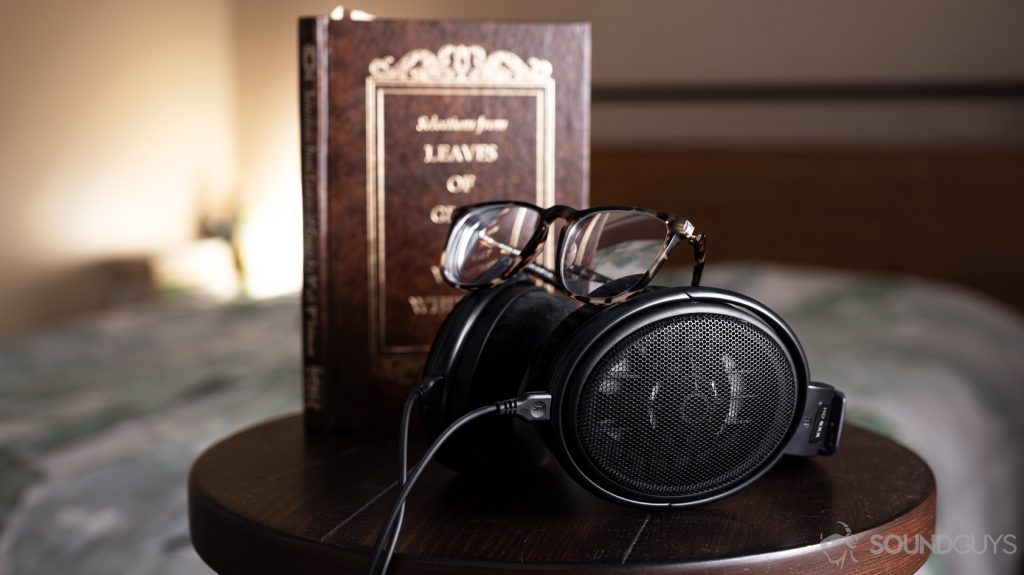 A picture of Warby Parker tortoise shell glasses on top of the Masdrop x Sennheiser HD 6XX open-back headphones on a stool in front of a book and bed.
