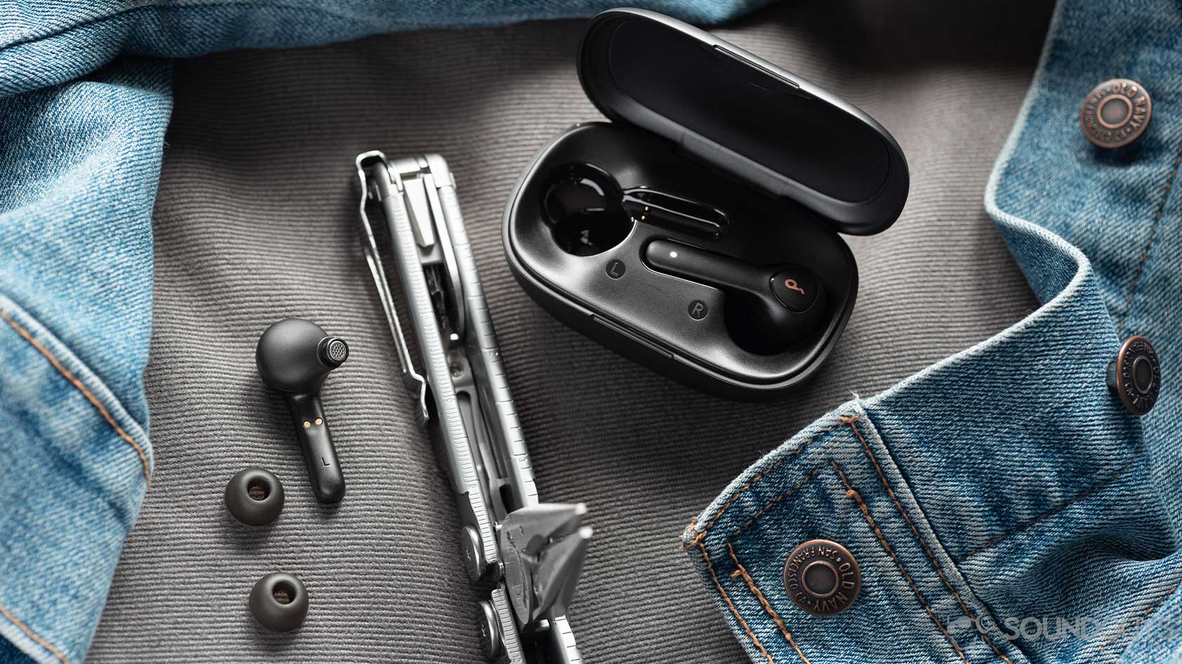 A picture of the Anker Soundcore Life P2 true wireless earbuds, ear tips, and case next to a Leatherman multitool and denim jacket.