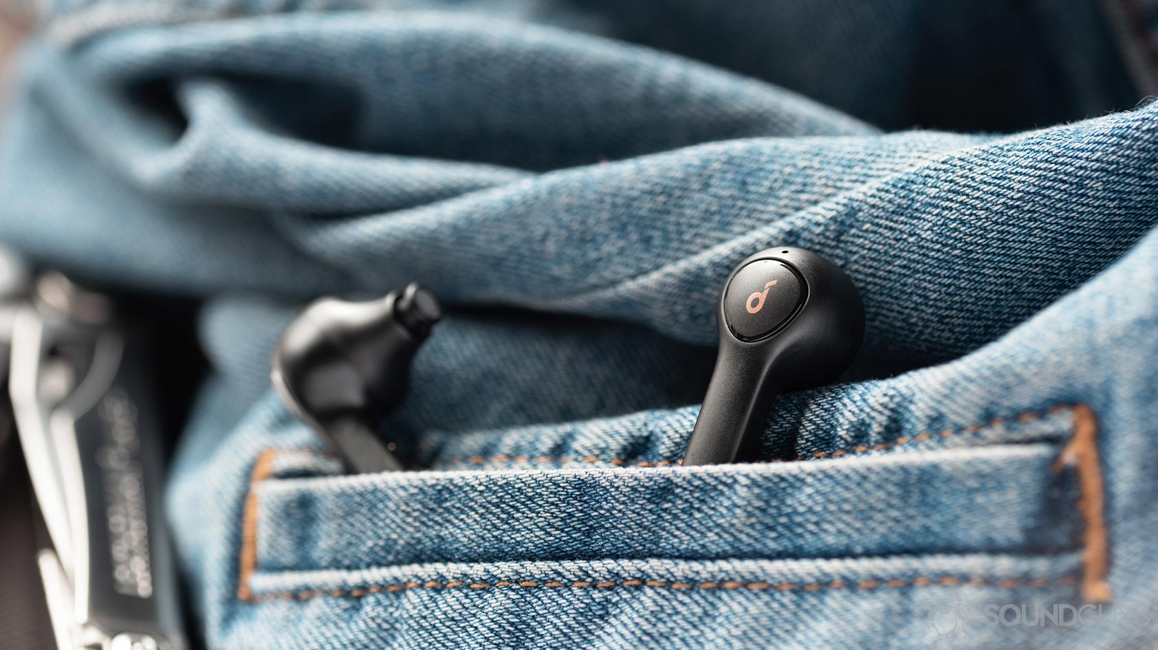 A picture of the Anker Soundcore Life P2 true wireless earbuds sticking out from a denim jacket pocket.
