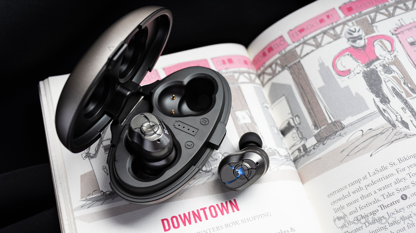 A photo of the HiFiMan TWS600 true wireless earbuds with one earbud in and the other out of the oblong open charging case on top of a book.