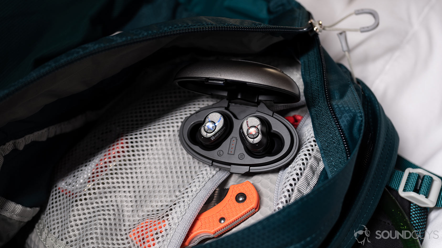 A photo of the HiFiMan TWS600 true wireless earbuds in the case with each LED indicator lit up, and the case is open in a backpack compartment.