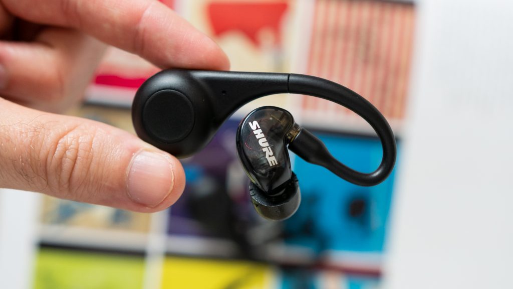 Man holding Shure Aonic 215 earbuds from the bulbous tip over colorful book