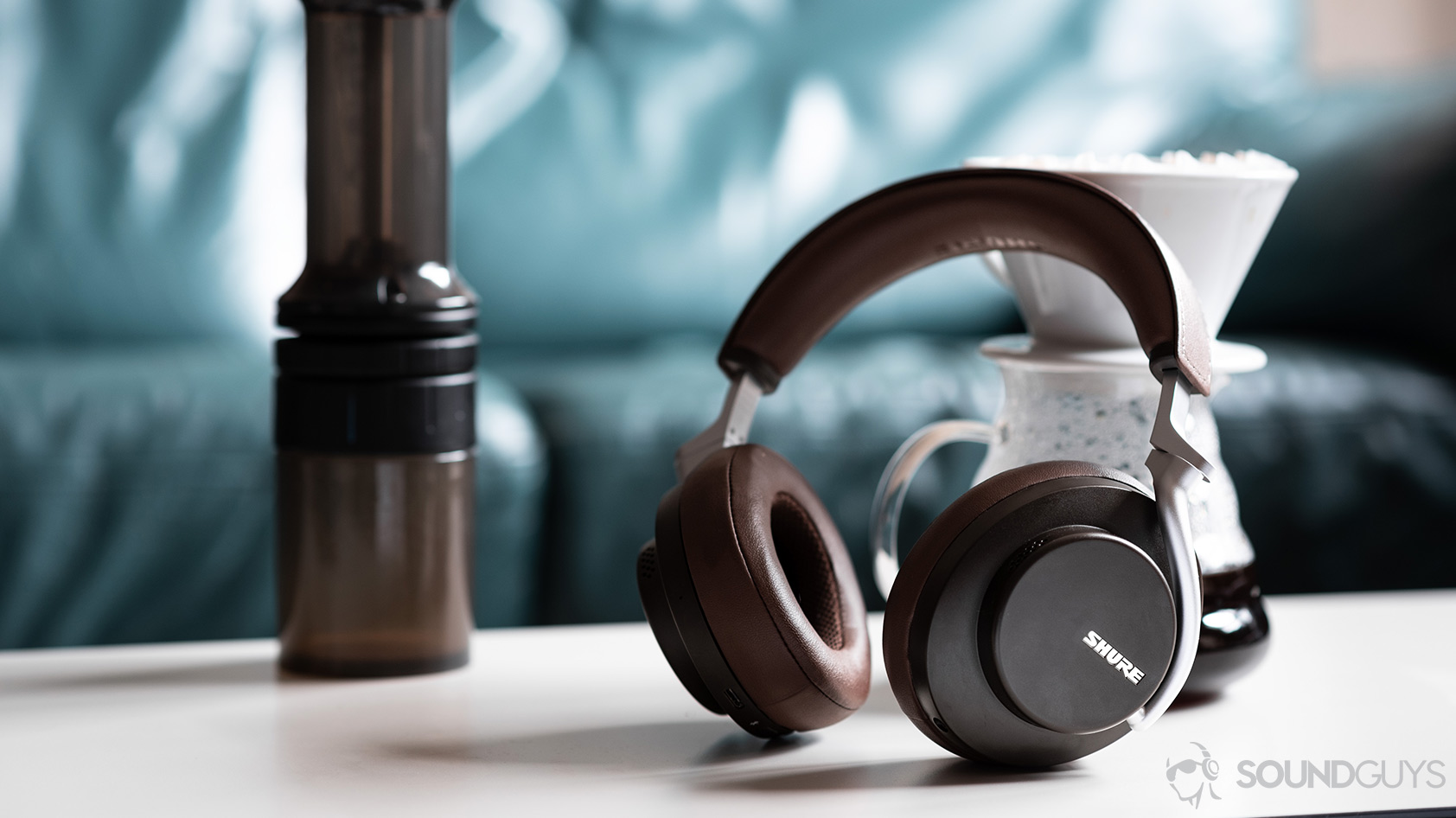The Shure AONIC 50 noise canceling headphones in brown leaning against a coffee carafe.