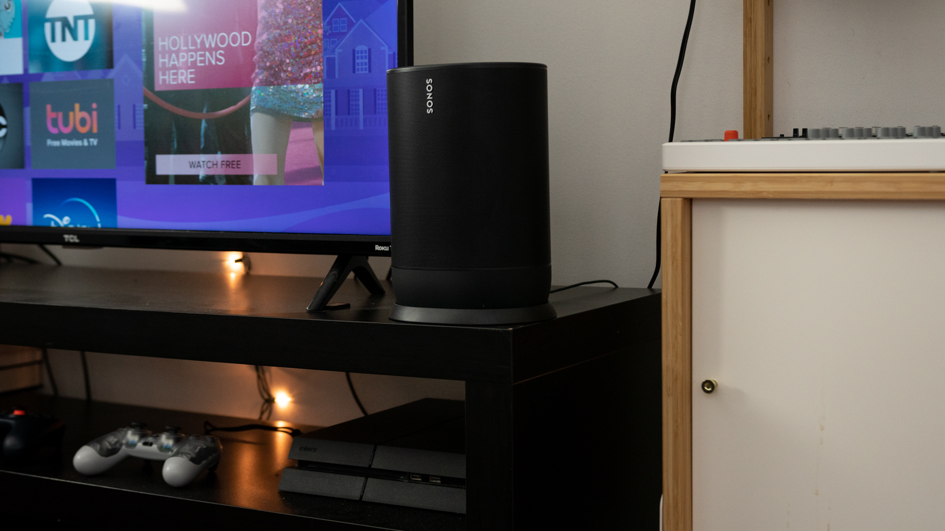 The Sonos Move speaker on a TV stand next to a Roku TV and a playstation controller