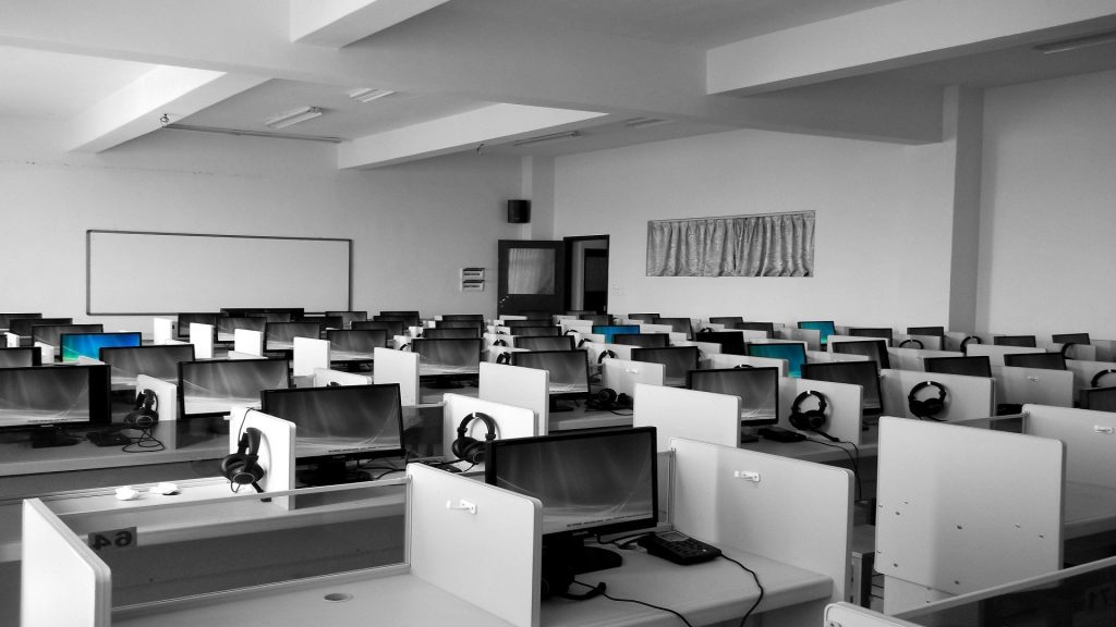 A photo of an empty call center, with headphones hanging by computers in small grey cubicles.