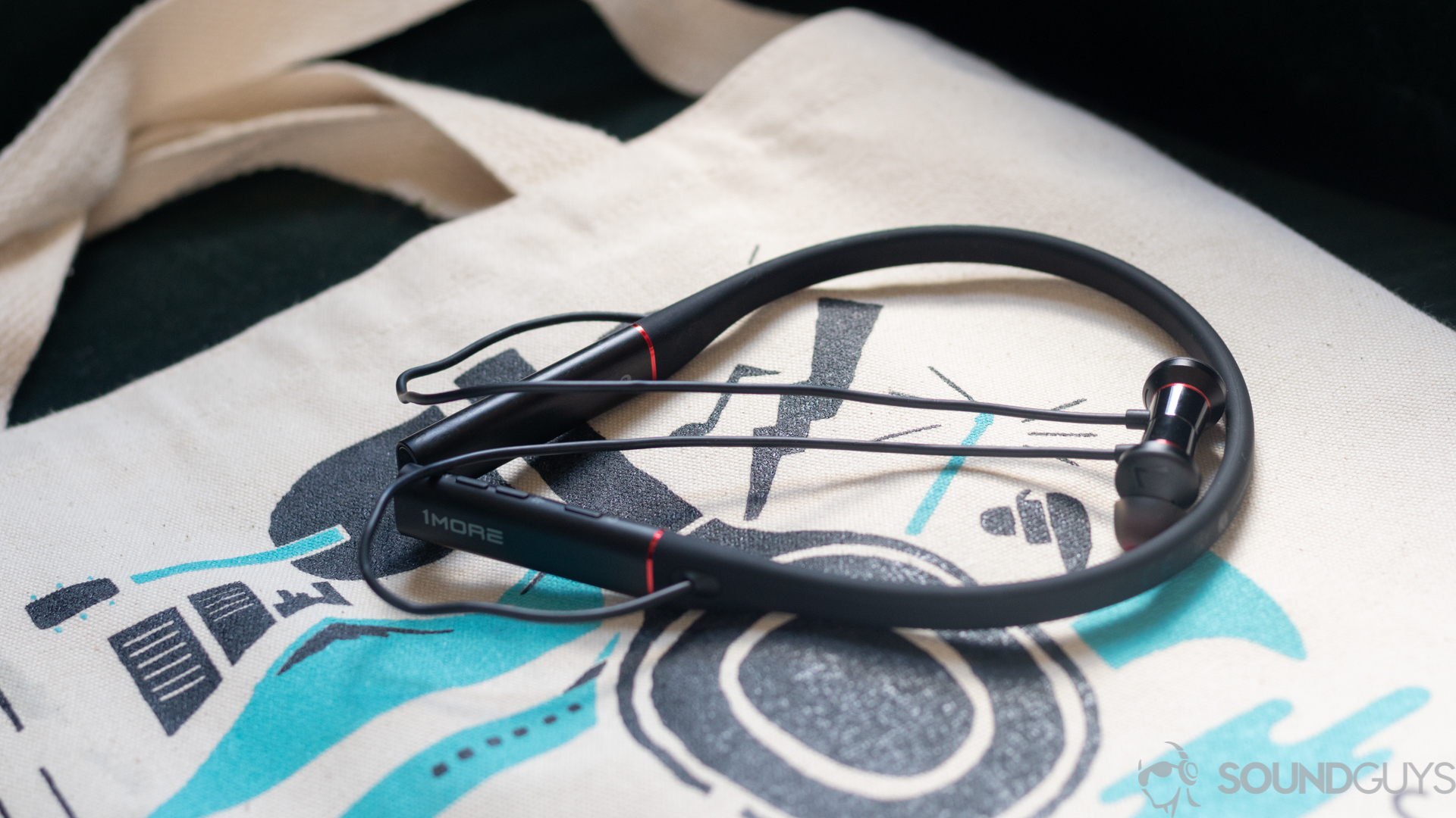 The 1More Dual Driver ANC Pro earbuds on top of a white tote bag with teal decorations.