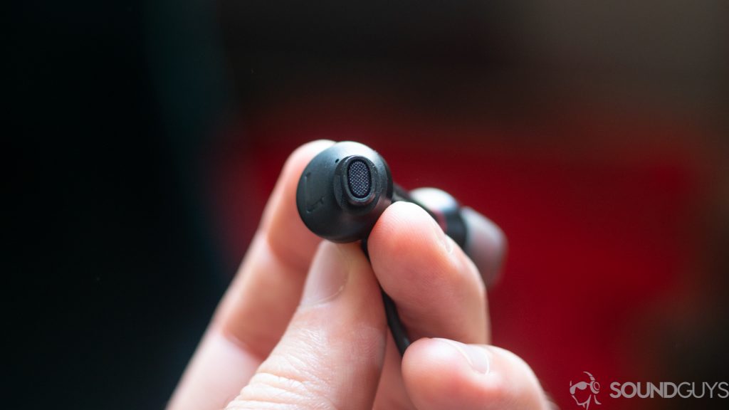 A picture of a man holding a single earbud of the 1More Dual Driver ANC Pro showing the oblong shape.