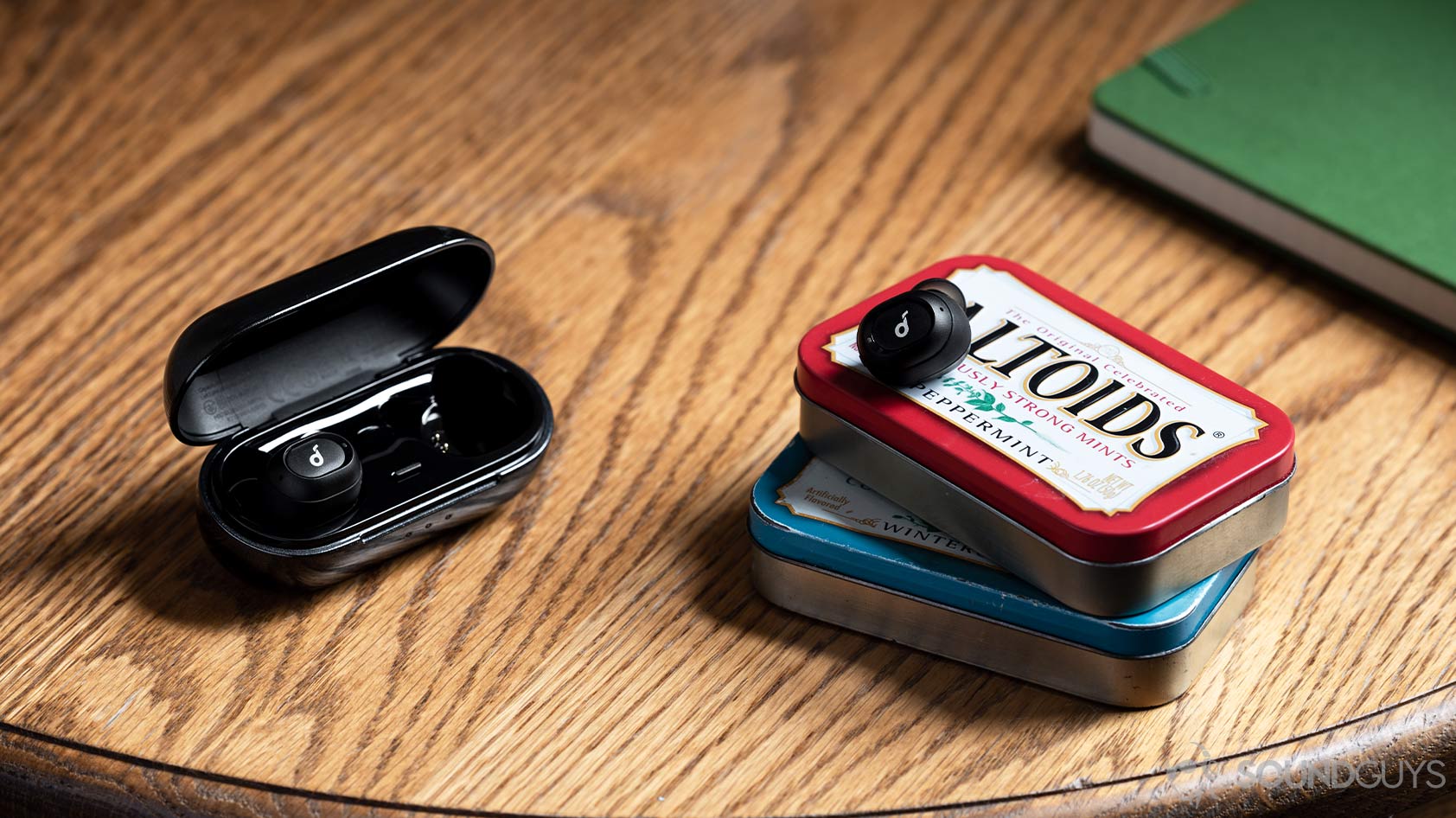A picture of the Anker SoundCore Liberty Neo true wireless earbuds with one in the charging case and the other atop two stacked Altoids tins.