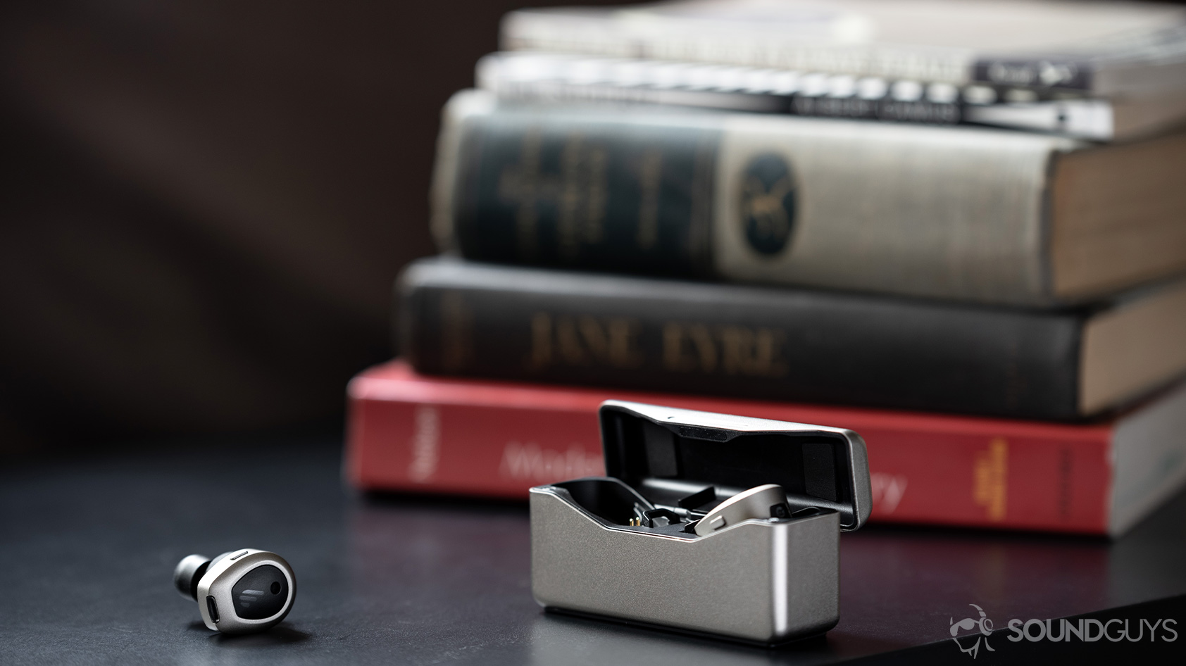 A picture of the Edifier TWS NB true wireless noise canceling earbuds, one in the open case and one outside of it, in front of a stack of books.