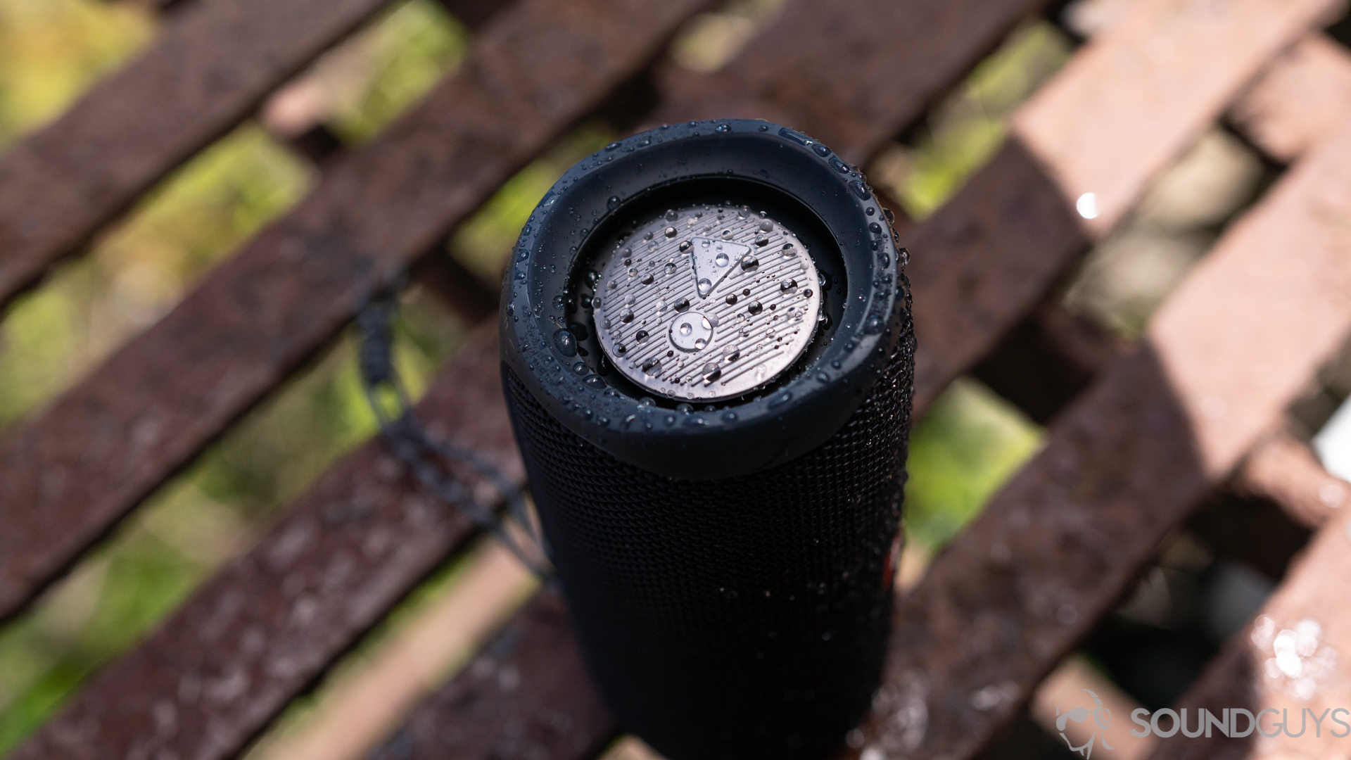 Pictured is the exposed bass radiator of the JBL Flip 5 on a fire escape with water on the speaker