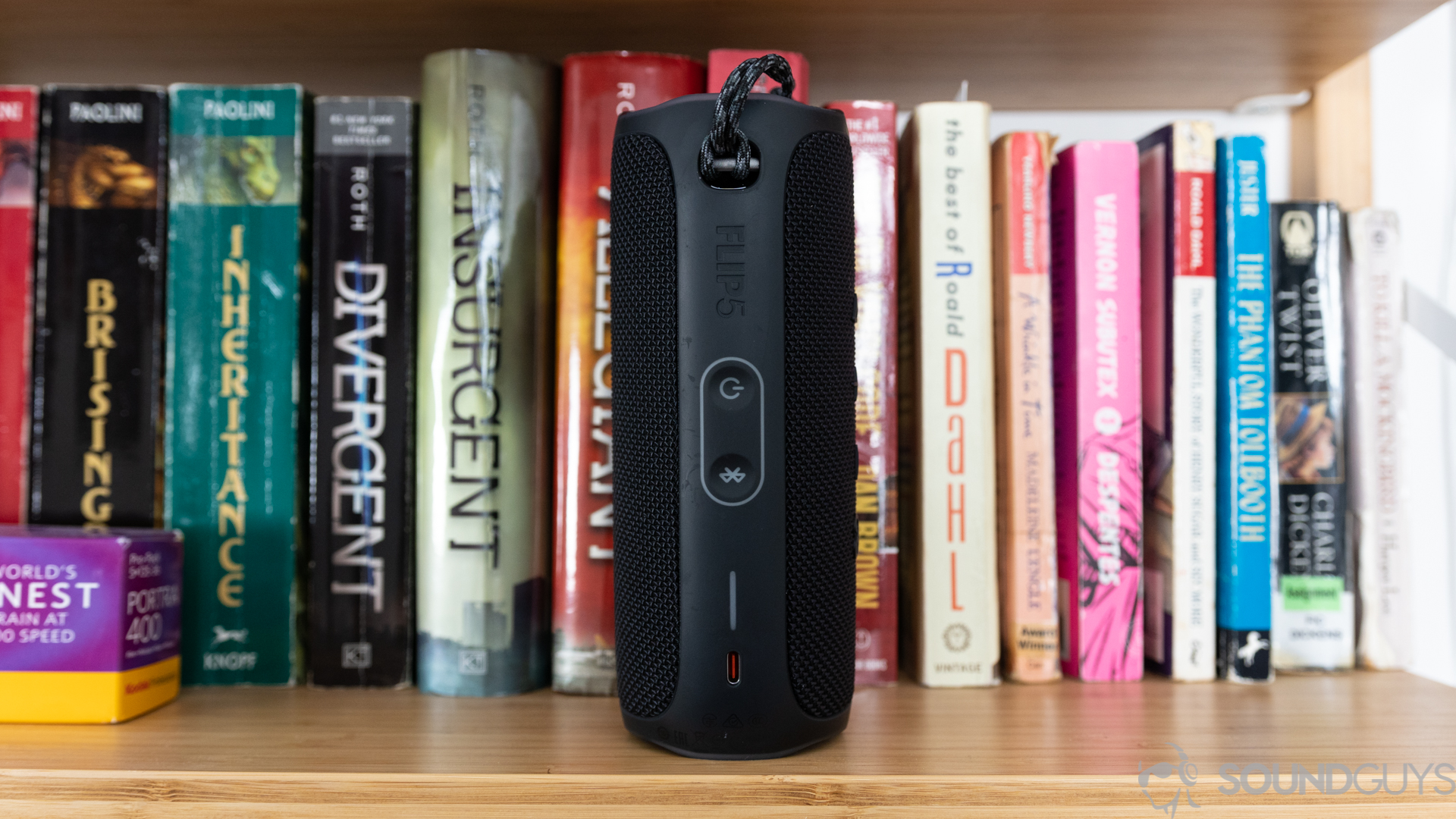 JBL Charge 5 on bookshelf with the power button Bluetooth buttons visible.