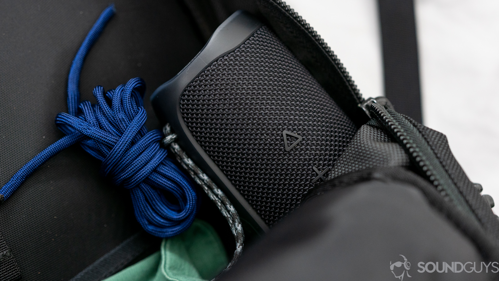 JBL Flip 5 next to blue paracord and green jacket in a black backpack