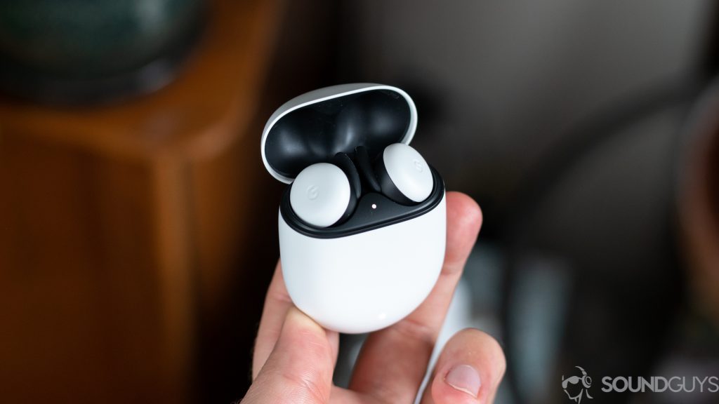 A picture of a man holding open charging case with new Pixel Buds inside with plant in background.