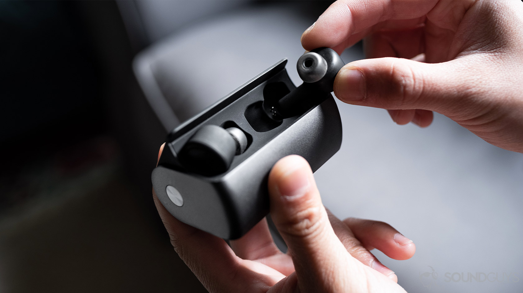 A picture of the RHA TrueConnect 2 case being held in a woman's hand as the other hand removes the far earbud.