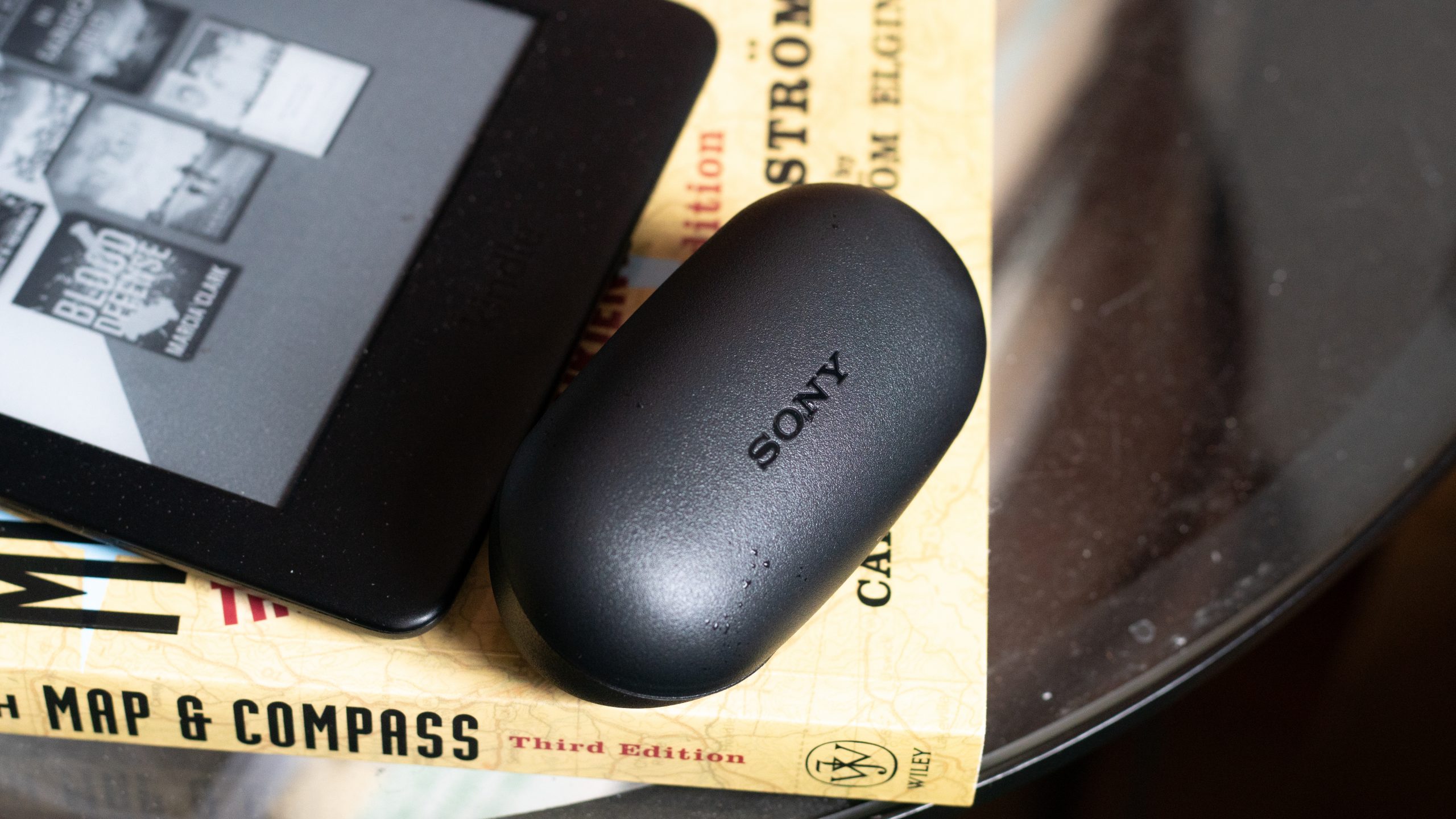 Sony WF-XB700 true wireless earbuds charging case on a book next to a kindle