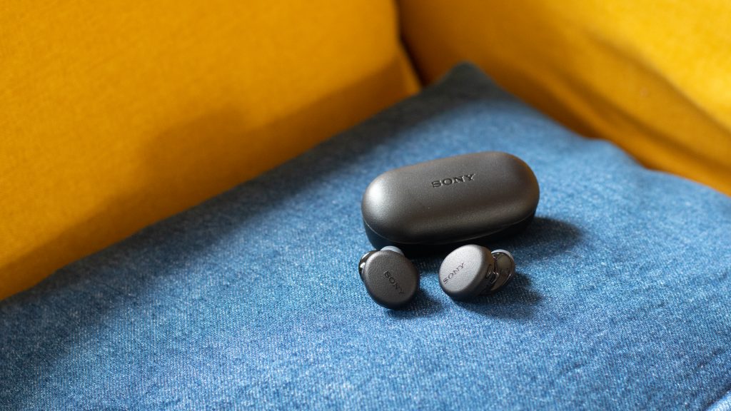 Sony WF-XB700 true wireless earbuds on a blue pillow with a yellow couch in the background